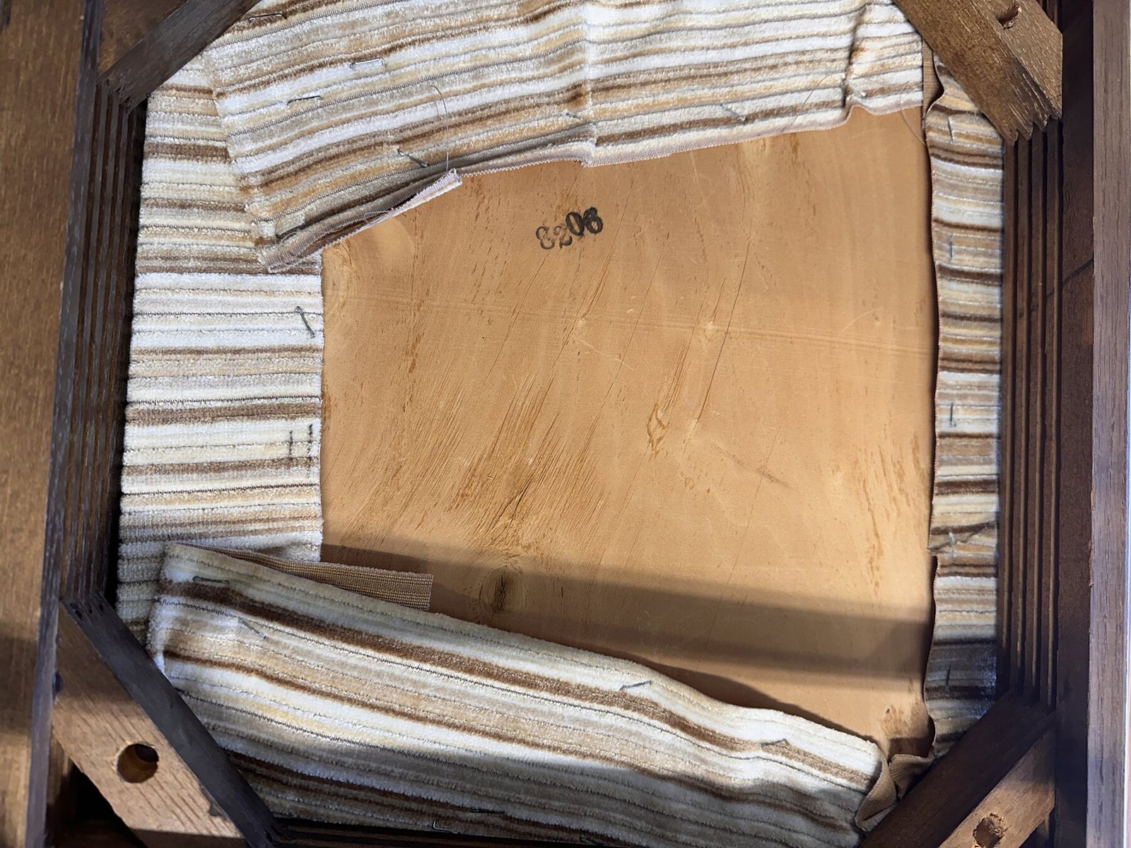 Underside of a chair seat showing wood frame, fabric, staples, and seat board