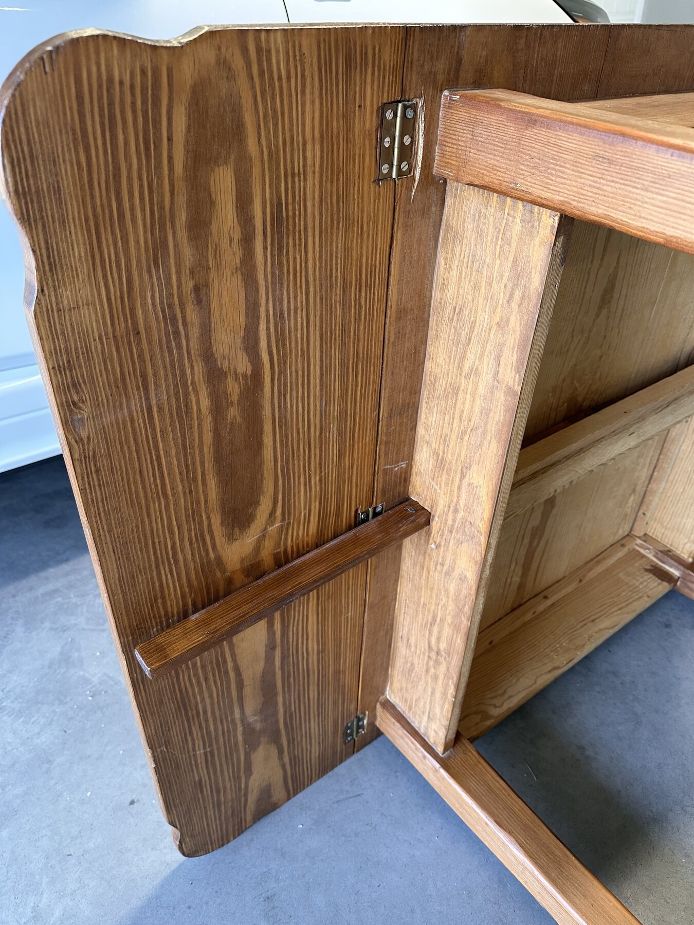 Underside of a raised drop leaf showing hinges and wooden support arm