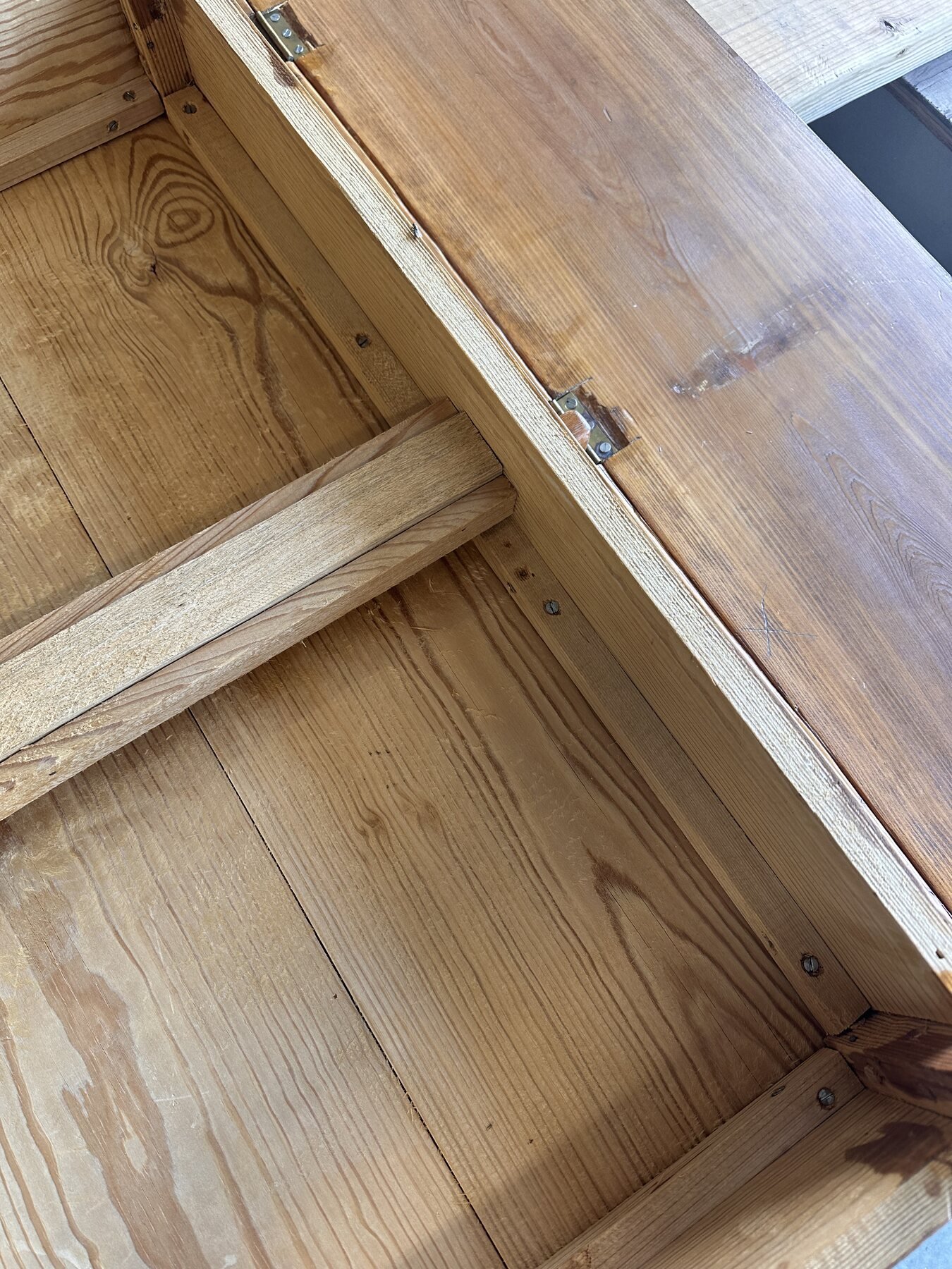 Underside view showing a wooden sliding brace, rail screws, and two drop-leaf hinges