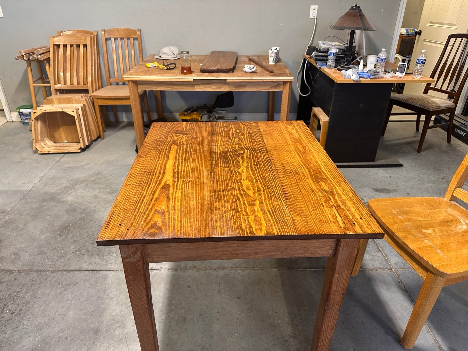 Front view of the first-coated tabletop above its apron and legs with other furniture behind it