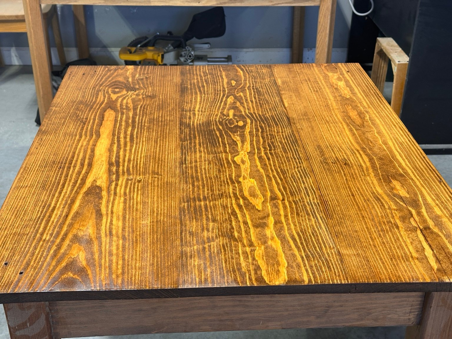 Front view across the center tabletop showing long golden grain lines beneath the first polyurethane coat
