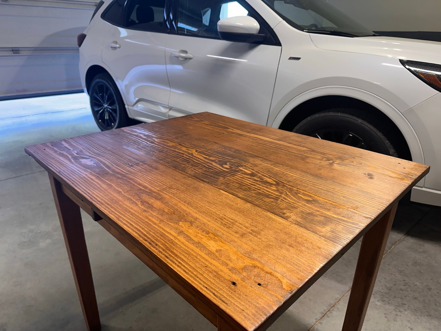 Drop-leaf table beside a white vehicle, viewed diagonally after the second polyurethane coat