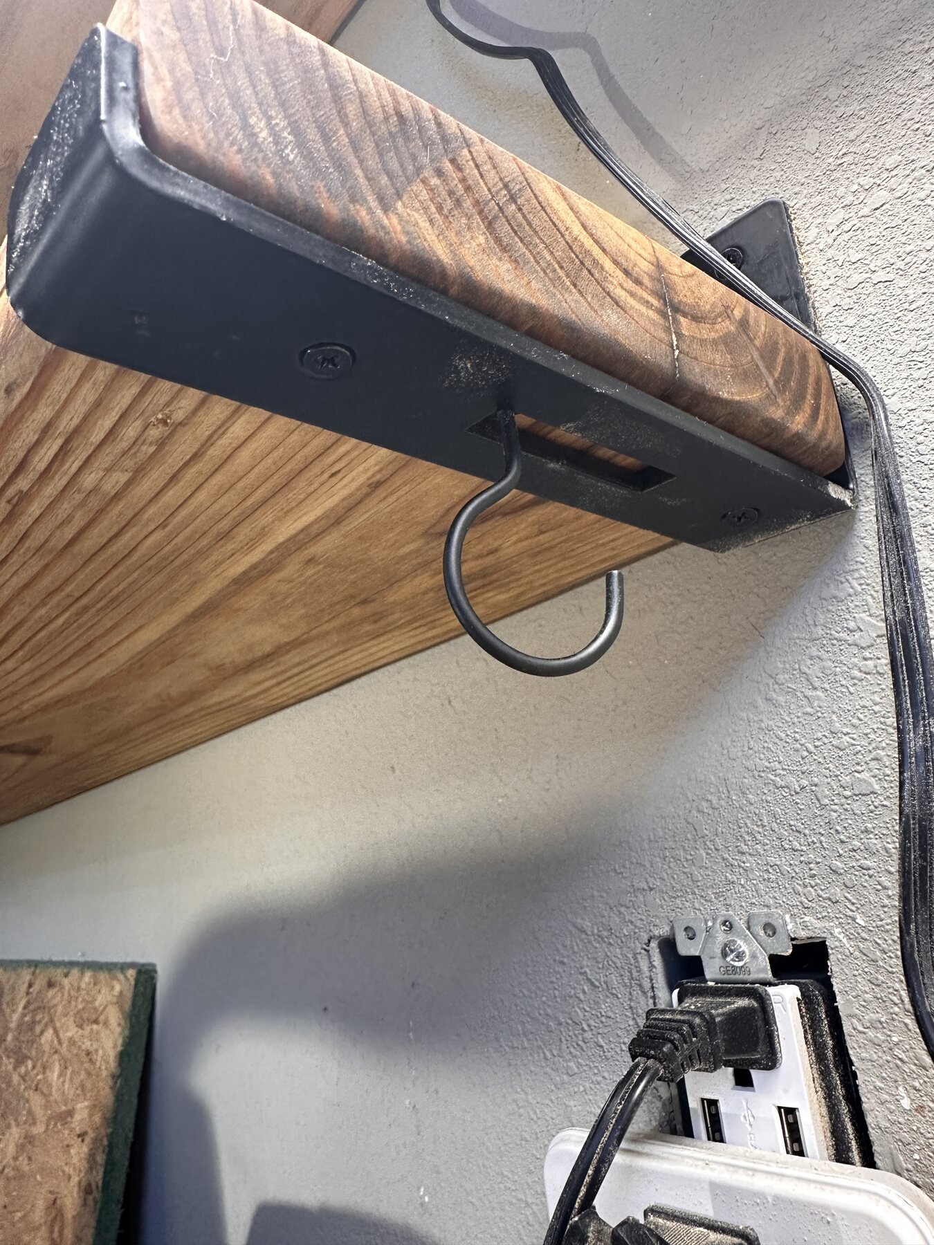 Underside view of bracket and finished pine shelf near wall outlet