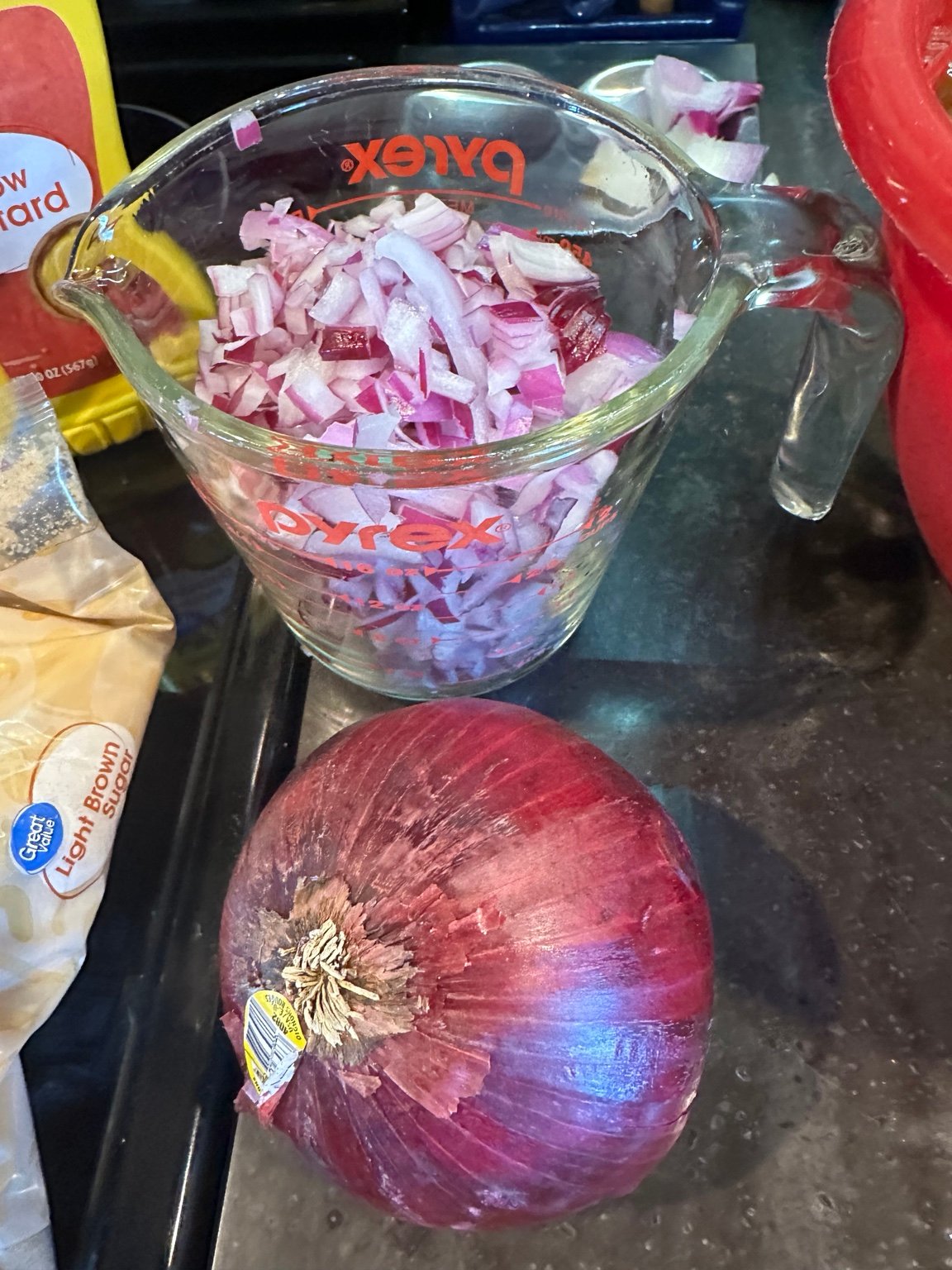 A measuring cup full of diced red onion beside a whole red onion