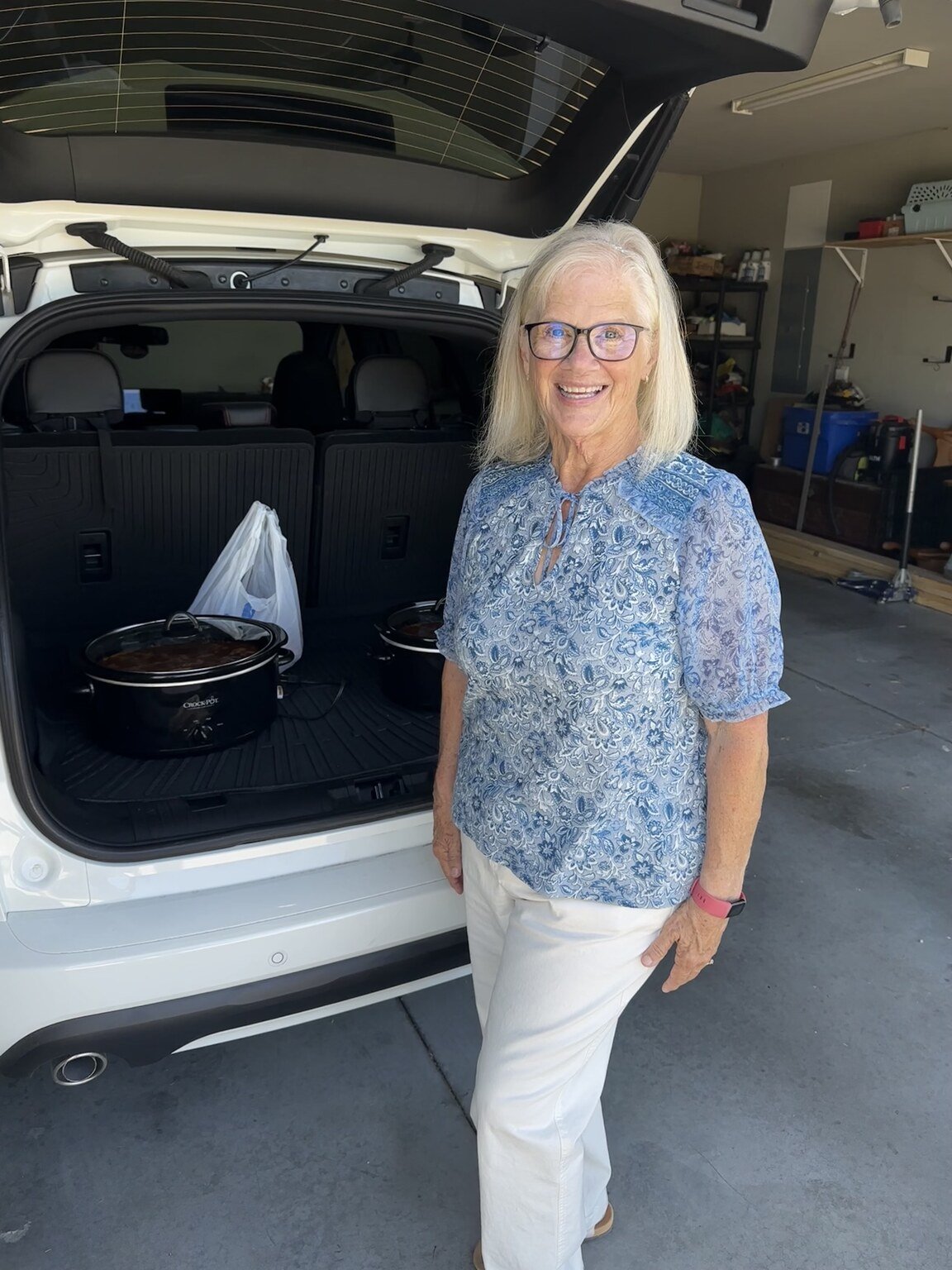 Janet smiling with her eyes open beside the car with two Crock-Pots of baked beans ready for a 50th anniversary party