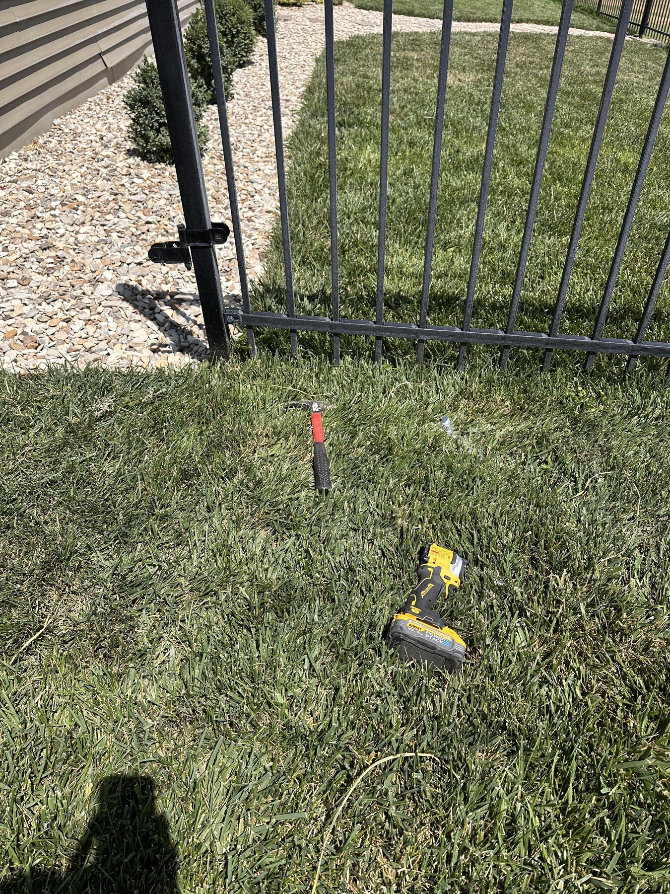 Cordless driver and hammer lying in the grass beside the open black gate