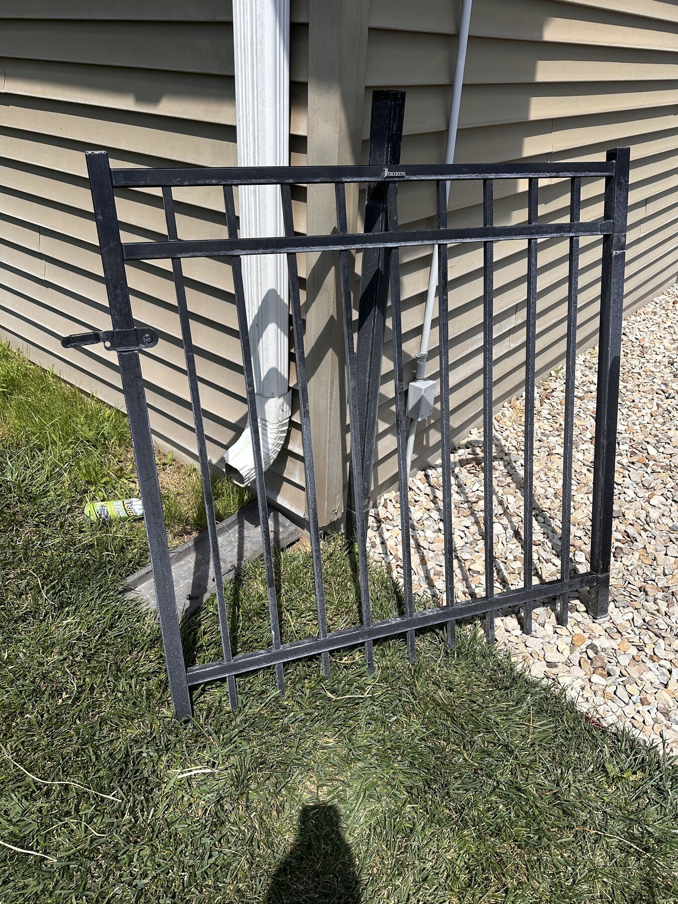 Black metal gate standing upright beside the house with its hardware reversed